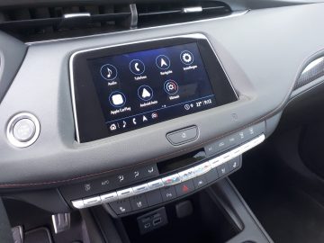 Het interieurdashboard van de Cadillac XT4 is voorzien van een touchscreen-display met opties voor audio, telefoon, navigatie en instellingen. Hieronder staan knoppen en draaiknoppen voor de klimaatregeling en andere functies.