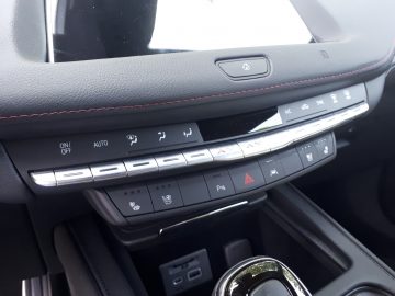 Een close-up van een Cadillac XT4-dashboard onthult klimaatcontroleknoppen, een alarmlichtknop en verschillende functiebedieningen. Het geavanceerde dashboard is voorzien van een combinatie van fysieke en aanraakgevoelige knoppen.