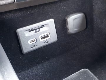 Close-up van het dashboardcompartiment van een Cadillac XT4 met USB Type-A-, USB Type-C-poorten en een SD-kaartsleuf.