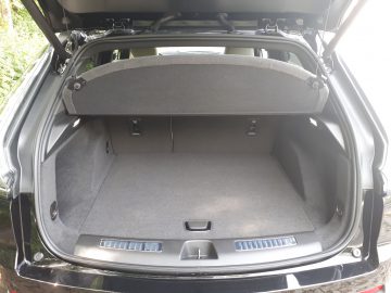 De open kofferbak van de Cadillac XT4 onthult een lege opbergruimte met vloerbedekking en de privacyafdekking op de achterbank omhoog.