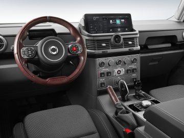 Binnenaanzicht van een modern Ineos Grenadier-dashboard met een centraal aanraakscherm, een multifunctioneel stuurwiel met knoppen en diverse bedieningsknoppen en knoppen op de middenconsole.