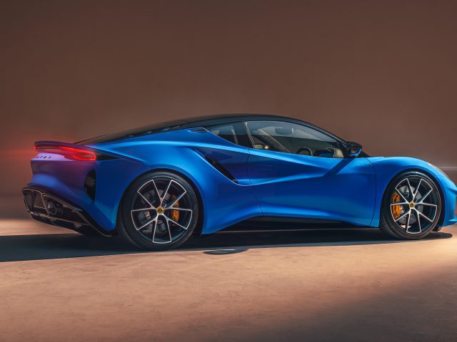 Op een gladde ondergrond staat een strakke, blauwe Lotus Emira met een aerodynamisch design en zwarte accenten, verlicht vanaf de zijkant.