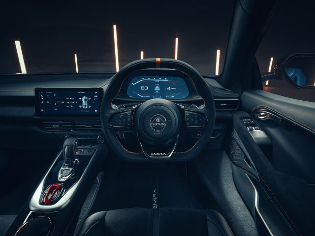 Het binnenaanzicht van de Lotus Emira heeft de esthetiek van een moderne sportwagen met een digitaal dashboarddisplay, een strak stuurwiel en een geavanceerd controlecentrum. LED-accenten verlichten de donkere cabine.