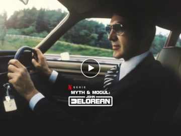 Een persoon bestuurt een auto en draagt een pak en stropdas. De autosleutels, met sleutelhanger, zijn zichtbaar in het contactslot. Tekstoverlay luidt "Myth & Mogul: John DeLorean" op Netflix.