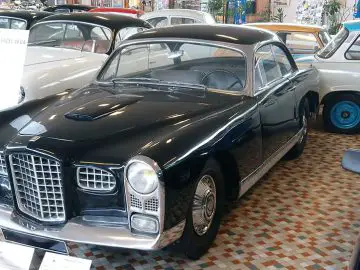 In het Musée Automobile de Vendée staat een vintage zwarte auto tentoongesteld, omringd door andere klassieke auto's op een geruite tegelvloer. Een bord bij de auto geeft informatie.