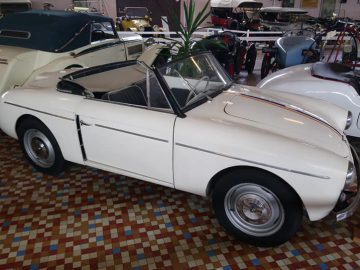 Een vintage witte cabriolet wordt tentoongesteld in een overdekte showroom in het Musée Automobile de Vendée, naast andere klassieke voertuigen.