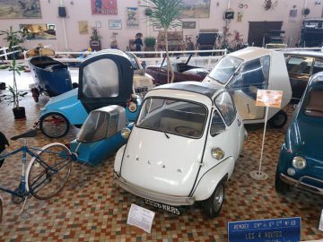 Een verzameling vintage brommobielen wordt tentoongesteld in het Musée Automobile de Vendée. De auto's staan op een tegelvloer met informatieborden voor elk voertuig, waardoor bezoekers fascinerende details over elk uniek model krijgen.