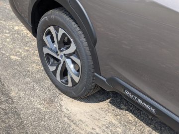 Close-up van het achterwiel en het zijembleem van een grijze Subaru Outback, geparkeerd op een betonnen ondergrond.