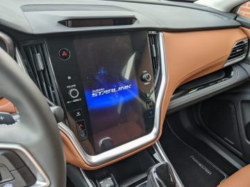 Binnenaanzicht van het dashboard van een Subaru Outback met een touchscreen-display met het Subaru STARLINK-logo, met omringende bedieningsknoppen en bruinleren accenten.