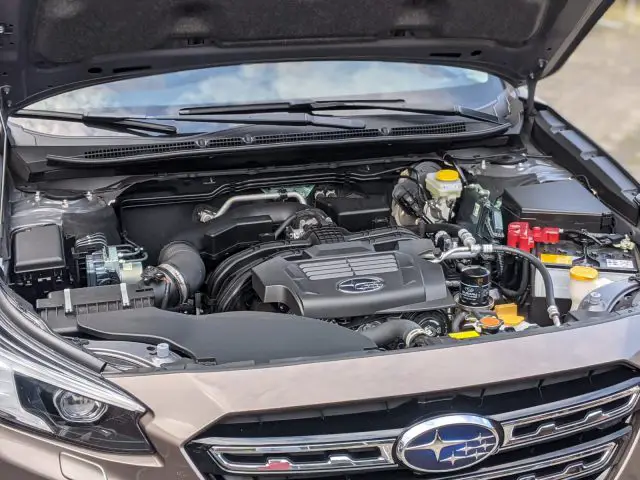 Een open autokap onthult de motorruimte van een Subaru Outback, met verschillende componenten en vloeistofreservoirs.