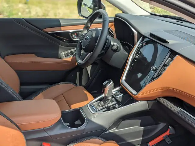 Interieur van een Subaru Outback met bruin lederen stoelen, zwart dashboard, groot touchscreen display, versnellingspook en stuur. Zonlicht is zichtbaar door de voorruit.