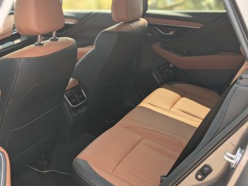 Binnenaanzicht van een Subaru Outback met twee voorstoelen en de achterpassagiersstoel in bruin lederen bekleding met zwarte accenten. De achterkant van de voorstoelen is voorzien van opbergvakken en ventilatieopeningen.