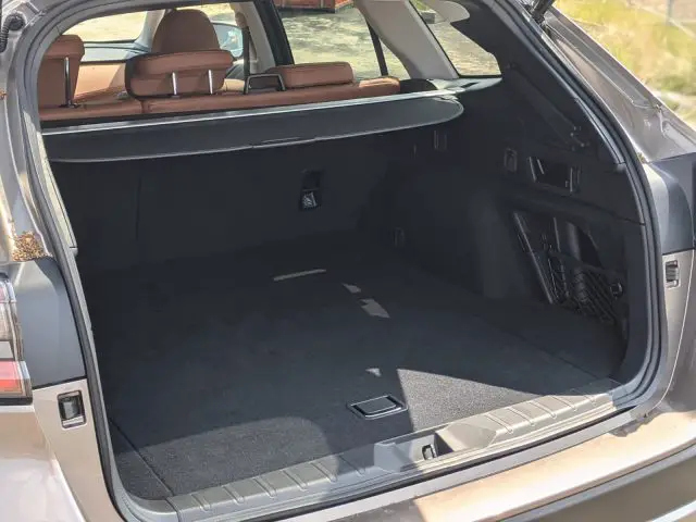 De afbeelding toont de open kofferbak van een Subaru Outback met een ruime lege ruimte, bruinleren stoelen neergeklapt en een intrekbare bagageafdekking die gedeeltelijk is uitgeschoven.