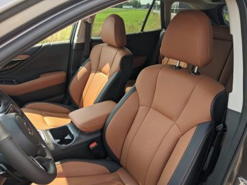 Binnenaanzicht van een Subaru Outback met bruinleren voorstoelen, middenconsole en een groen veld zichtbaar buiten het raam.