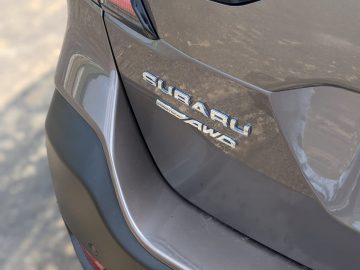 Close-up van de achterkant van een beige Subaru Outback-auto met de kenmerkende "Subaru"- en "AWD"-badges.