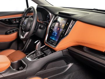 Modern auto-interieur met oranje en zwart kleurenschema, een groot touchscreen-infotainmentsysteem en een strakke versnellingspook op een middenconsole, net als in de nieuwste Subaru Outback.