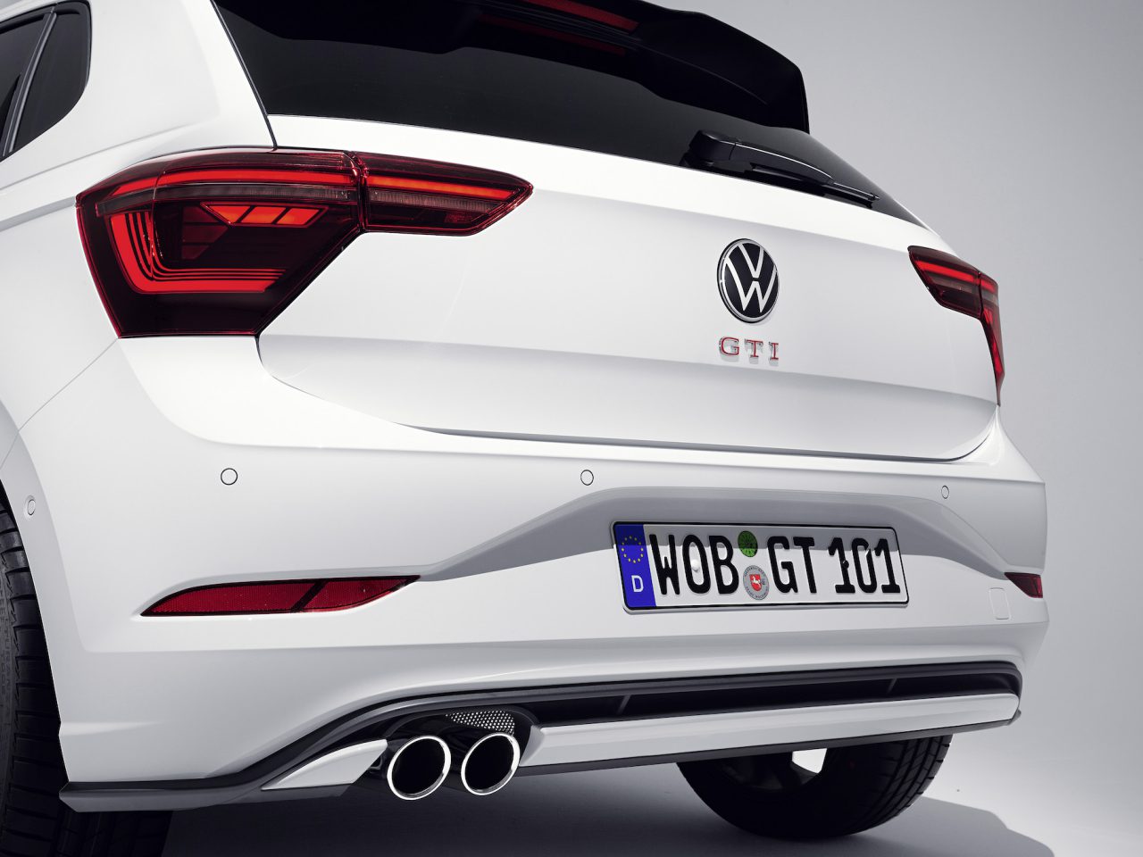 Close-up van de achterkant van een witte Volkswagen Polo GTI. De afbeelding toont het GTI-embleem, achterlichten, dubbele uitlaatpijpen en een Europees kenteken.