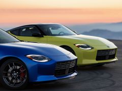 Twee sportwagens, een blauwe en een gele Nissan Z, geparkeerd op een bergweg bij zonsondergang met een schilderachtige achtergrond.