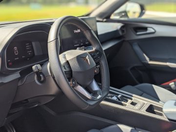 Close-up van een modern Cupra Formentor-interieur, met een multifunctioneel stuur met het Cupra-logo, een digitaal instrumentenpaneel en een middenconsole met verschillende bedieningsknoppen en een versnellingspook.