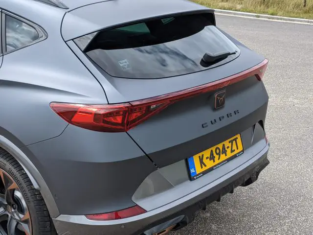 Het achteraanzicht van een grijze CUPRA Formentor, voorzien van een Nederlands kenteken K-494-ZT, toont zijn strakke achterlichten en moderne design, geparkeerd op een weg.