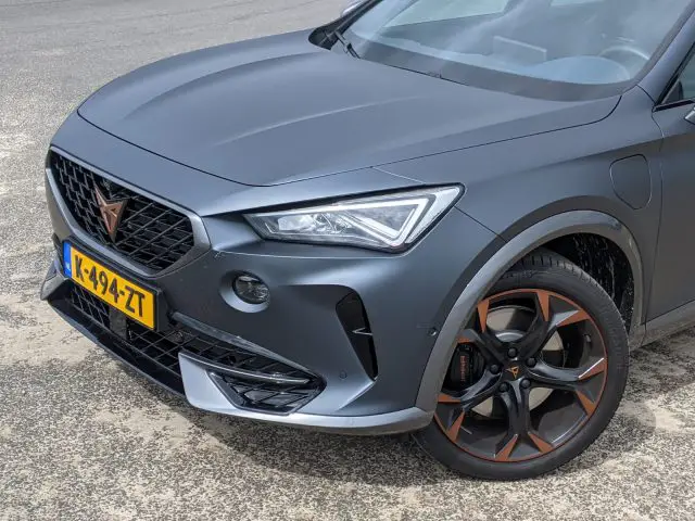 Close-up van de voorkant van een donkergrijze Cupra Formentor SUV met Nederlands kenteken, voorzien van opvallende lichtmetalen velgen en een strak koplampontwerp.