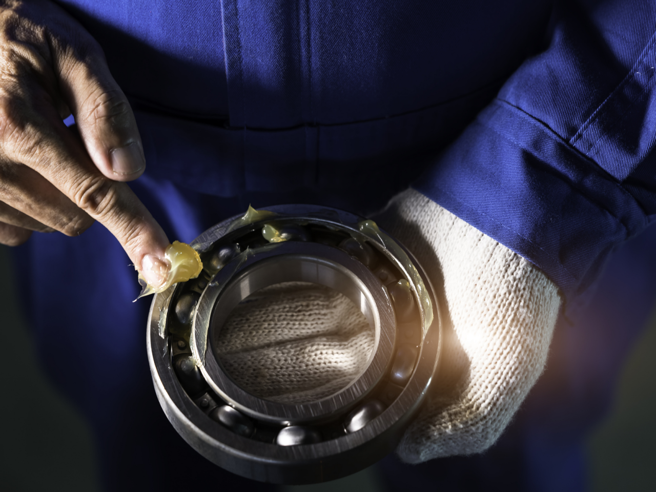 Een persoon in een blauw uniform en witte handschoen gebruikt zijn vinger om smeermiddel op een goede wiellager aan te brengen, waardoor de soepele werking en lange levensduur ervan wordt gegarandeerd.