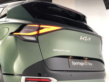 Achteraanzicht van een groene Kia Sportage GT-line SUV met verlichte achterlichten en het opvallende Kia-logo dat helder schijnt.