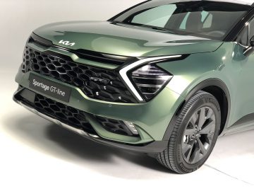 Close-up vooraanzicht van de groene Kia Sportage GT-line SUV, met de moderne grille, het koplampontwerp en het merkembleem.