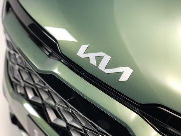 Close-up van de grille van een groene Kia Sportage met het Kia-logo.