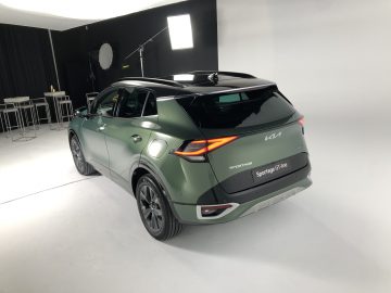 Een groene Kia Sportage G-line auto staat elegant in een studio, verlicht door professionele verlichting tegen een smetteloos witte achtergrond.