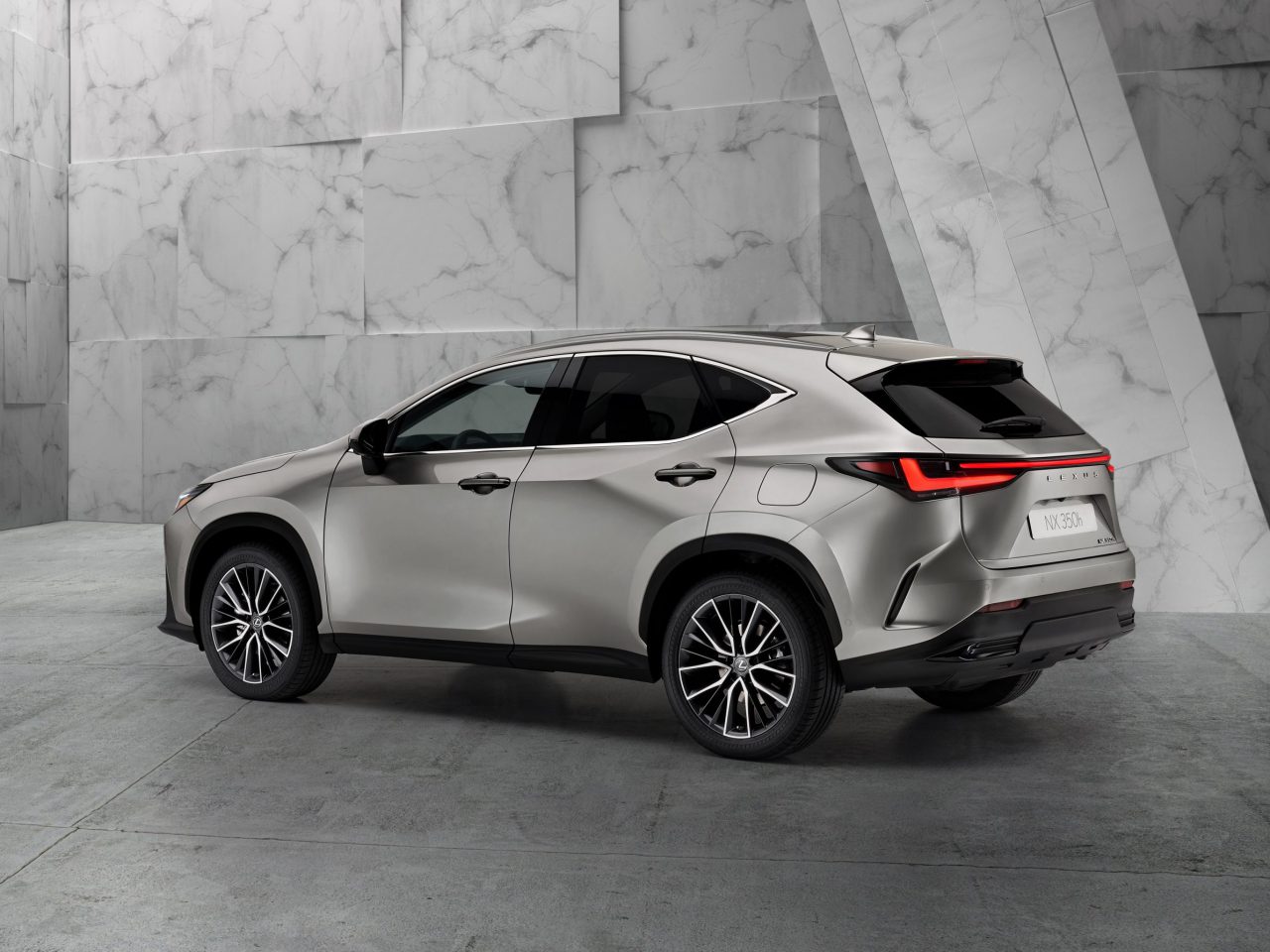 Een Lexus NX SUV, geparkeerd in een lege, moderne binnenruimte van beton en marmer, gezien vanaf de achterkant.