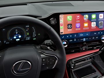 Een auto-interieur met een digitaal instrumentenpaneel achter het stuur en een centraal touchscreen op het dashboard met Apple CarPlay. Het Lexus-logo is prominent aanwezig op het stuur en onderstreept het verfijnde ontwerp van de Lexus NX.