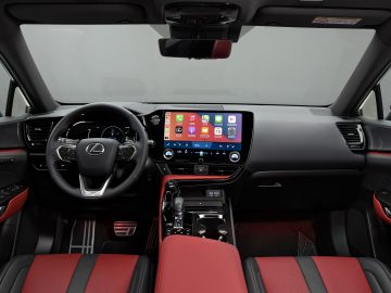 Binnenaanzicht van een Lexus NX met een strak dashboard met een groot aanraakscherm, een stuurwiel en rode en zwarte lederen stoelen.