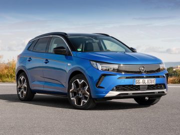 Een blauwe Opel Grandland SUV staat geparkeerd op een verhard oppervlak in een buitenomgeving, terwijl het strakke ontwerp glanst onder een blauwe lucht vol wolken.