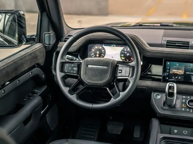 Close-up van het moderne dashboard van een auto met een digitaal instrumentenpaneel, multifunctioneel stuurwiel en touchscreenbediening. Het interieur, dat doet denken aan de stijl van Winston Gerschtanowitz, is ontworpen met zwart leer en metallic accenten.