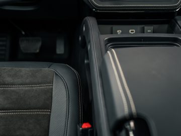 Close-up van het interieur van een auto, met een deel van de bestuurdersstoel, de middenconsole met stiksel en de pedalen – ontworpen met de precisie waar zelfs Winston Gerschtanowitz indruk op zou maken.