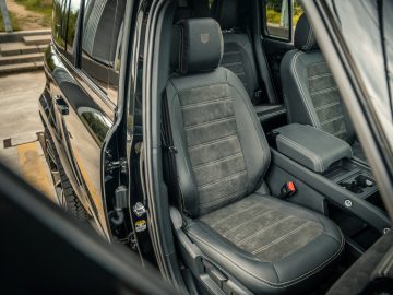 Een afbeelding van het interieur van een voertuig met stoelen van leer en suède, waarbij de nadruk ligt op de bestuurders- en passagiersstoelen voorin. Het bestuurdersportier staat open, waardoor er duidelijk zicht is op de stoelen en de middenconsole, wat een gevoel van luxe oproept dat Winston Gerschtanowitz zelf op prijs zou stellen.