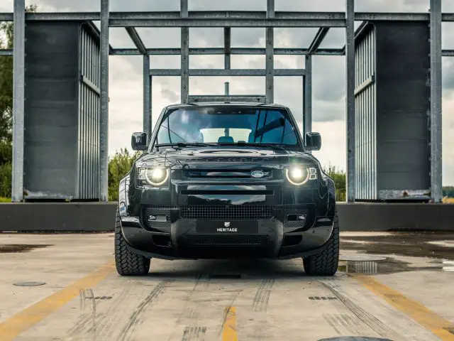 Een zwarte SUV, die doet denken aan de stijl van Winston Gerschtanowitz, staat geparkeerd op een betonnen oppervlak tussen metalen constructies onder een bewolkte hemel.