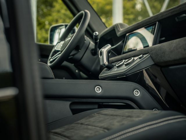 Binnenaanzicht van een auto met het stuur, het dashboard en het moderne touchscreen-display. Zwart lederen stoelen en metalen accenten zijn prominent aanwezig en weerspiegelen de verfijnde smaak van Winston Gerschtanowitz.