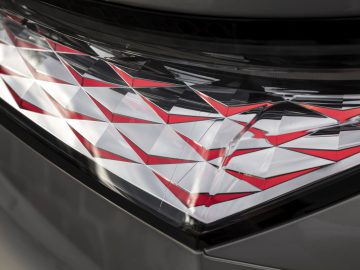 Close-up van het achterlicht van een DS 4 met een ingewikkeld geometrisch ontwerp met rode en witte delen. Het ontwerp creëert een driedimensionaal, reflecterend patroon.