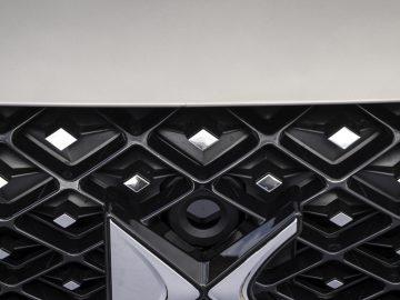 Close-up van de grille van een auto met een opvallend DS Automobiles-logo en een kleiner logo met een vlagmotief erboven. Het geometrische, ruitachtige patroon van de grille verwijst naar het verfijnde design van de DS 4.