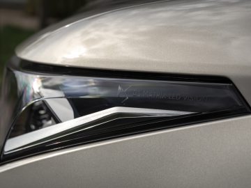 Close-up van de koplamp van een DS 4 met de tekst "DS MATRIX LED VISION" erin gegraveerd, met een metallic zilveren carrosserie zichtbaar op de achtergrond.