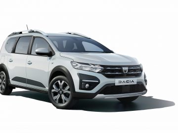 Een witte Dacia Jogger wordt linksvoor getoond op een effen witte achtergrond. De auto heeft een modern design met zwarte accenten en lichtmetalen velgen, wat de stijlvolle uitstraling benadrukt.