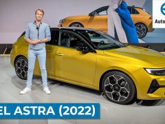 Een persoon staat naast een felgele Opel Astra (2022) op een podium. Het logo ‘AutoRAI.nl’ en de tekst ‘OPEL ASTRA (2022)’ zijn prominent weergegeven. Op de achtergrond wordt op een groot scherm nog een afbeelding van de gestroomlijnde Opel Astra getoond.