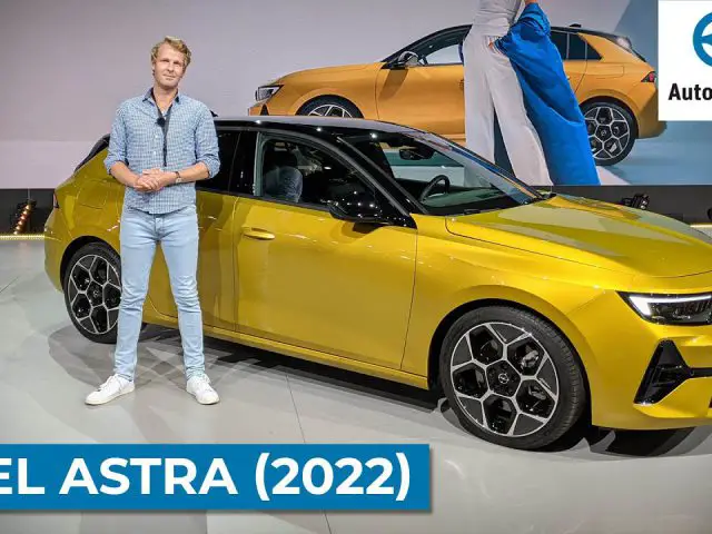 Een persoon staat naast een felgele Opel Astra (2022) op een podium. Het logo ‘AutoRAI.nl’ en de tekst ‘OPEL ASTRA (2022)’ zijn prominent weergegeven. Op de achtergrond wordt op een groot scherm nog een afbeelding van de gestroomlijnde Opel Astra getoond.