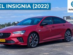 Een strakke rode Opel Insignia GSi uit 2022 staat geparkeerd op een verhard oppervlak op een industrieterrein.
