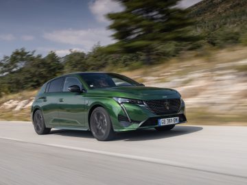 Een groene Peugeot 308 die over een weg rijdt met bomen en heuvels op de achtergrond.