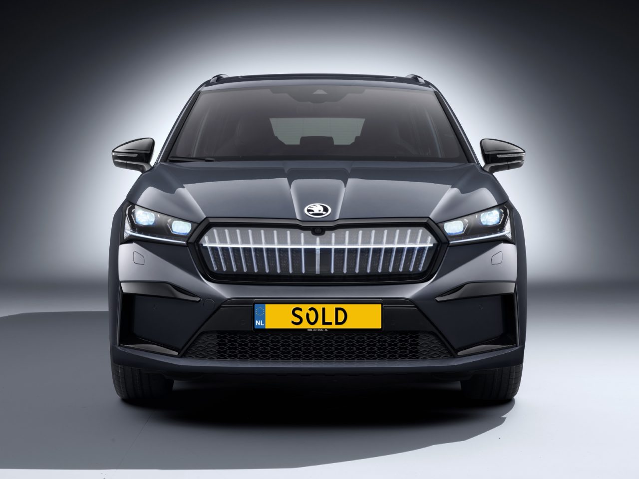 Vooraanzicht van een donkergekleurde SUV met verlichte koplampen, waarop een geel "VERKOCHT" kenteken staat, ter markering van de autoverkoop augustus 2021.