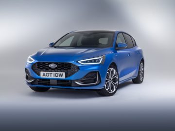 Een blauwe Ford Focus hatchback met kenteken "AOT IOW" wordt getoond in een studiosetting met een verloopachtergrond.