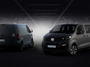 Twee donkergrijze Fiat Scudo-busjes staan binnen geparkeerd in een slecht verlichte ruimte. Het busje aan de linkerkant is van achteren weergegeven, terwijl het busje aan de rechterkant naar voren is gericht. Beide voertuigen zijn voorzien van heldere koplampen.